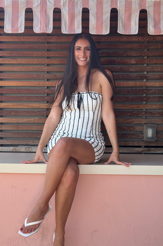 Woman in a striped swimsuit sitting on a ledge with a wooden wall and pink canopy in the background
