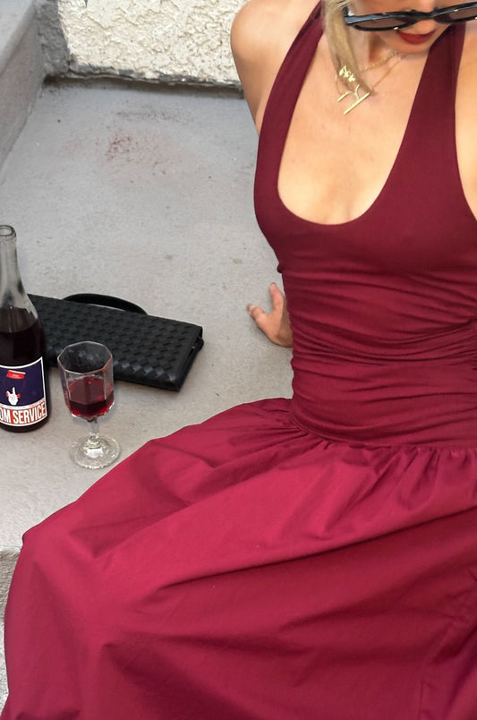 Person wearing a burgundy dress sitting on steps with a bottle and glass of red wine.