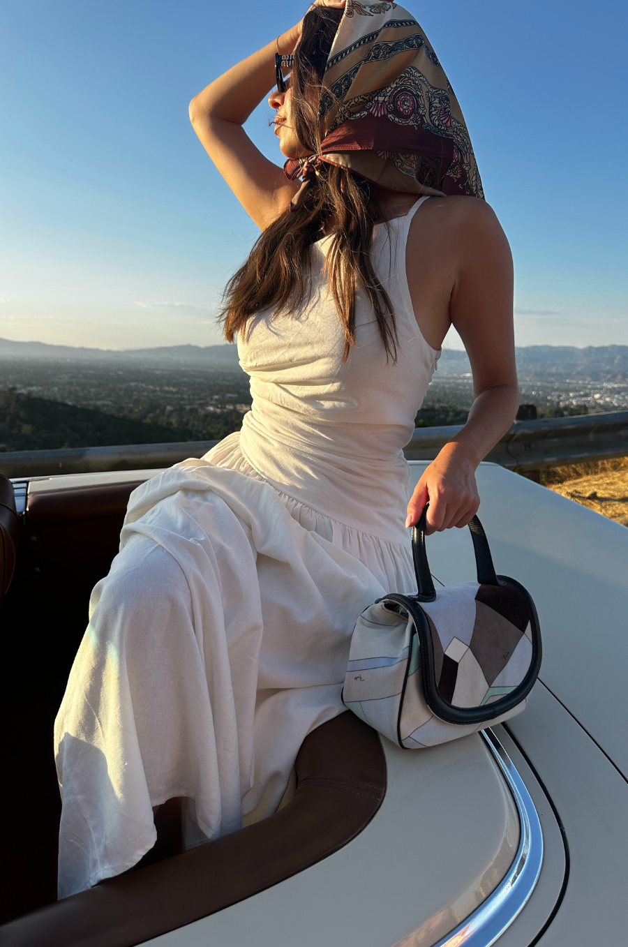 Woman in a white dress sitting on a vehicle with a scenic background
