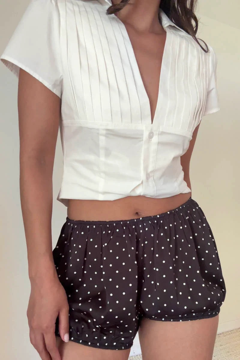 Person wearing a white blouse and polka dot shorts on a plain background