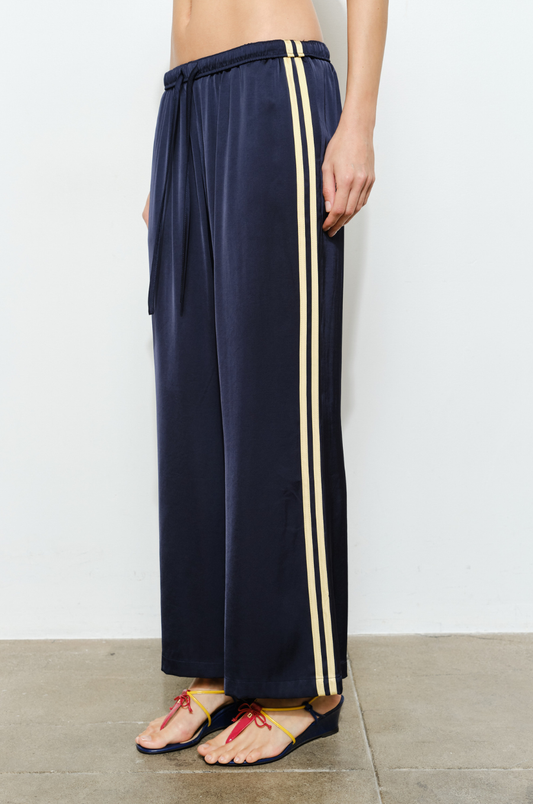 Navy blue wide-leg pants with yellow stripes worn by a person on a light gray background