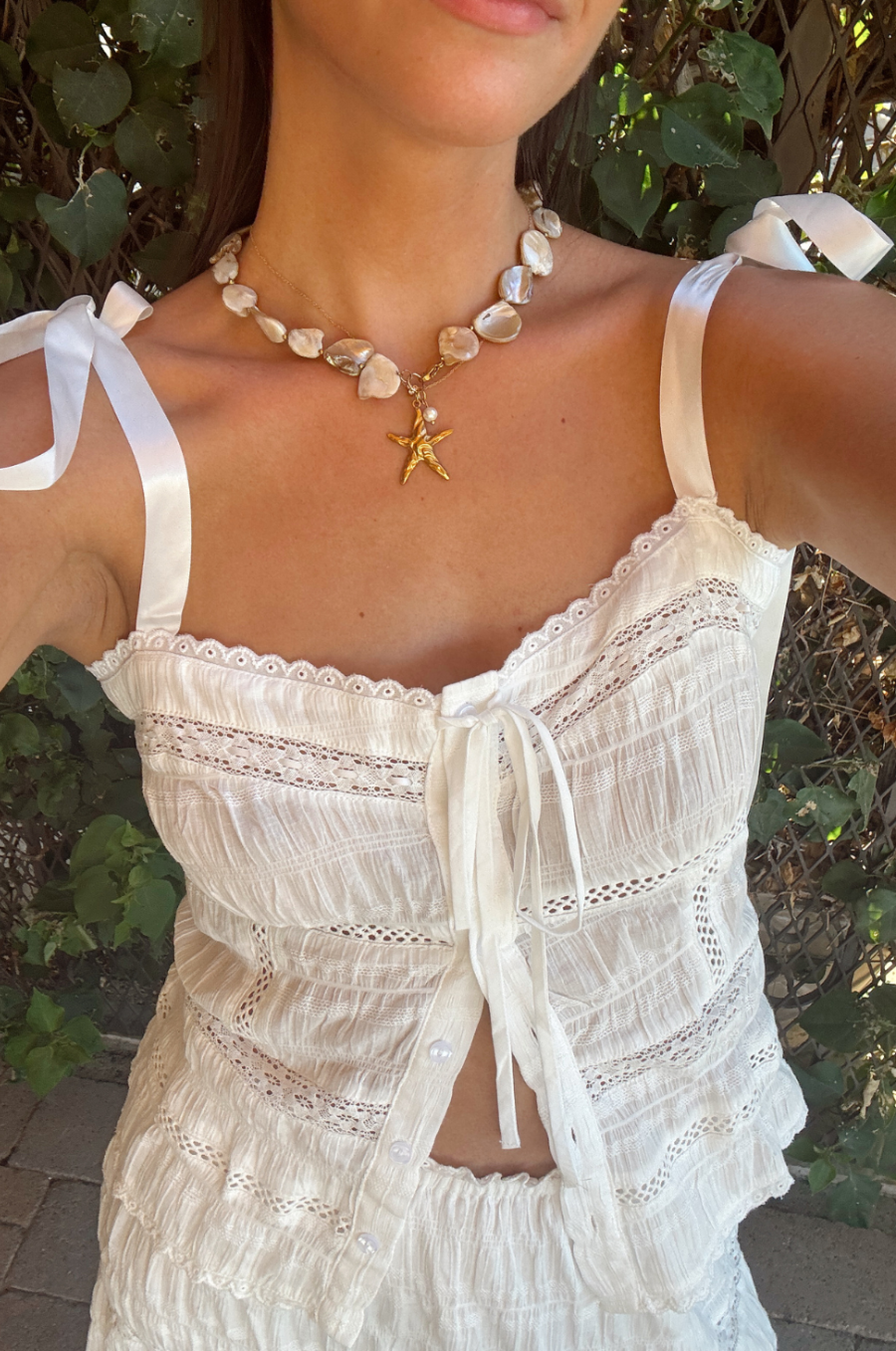 Woman wearing a white lace top with starfish necklace in a natural setting