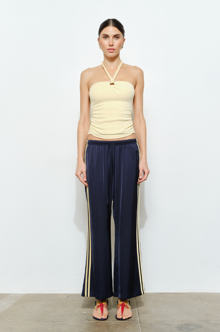 Woman wearing a yellow top and navy pants with gold stripes against a white background