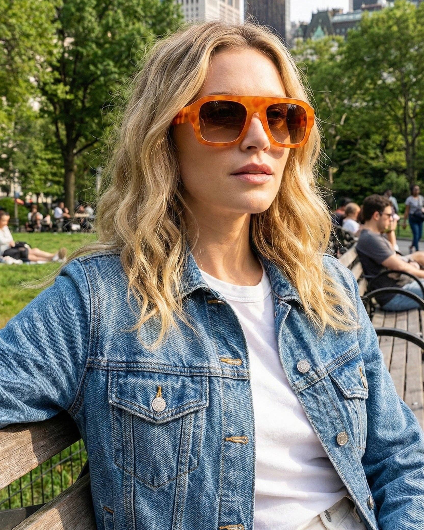 Woman wearing orange sunglasses and a denim jacket in a park setting