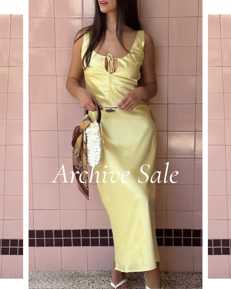 Woman in a yellow dress standing against a pink tiled wall with 'Archive Sale' text.