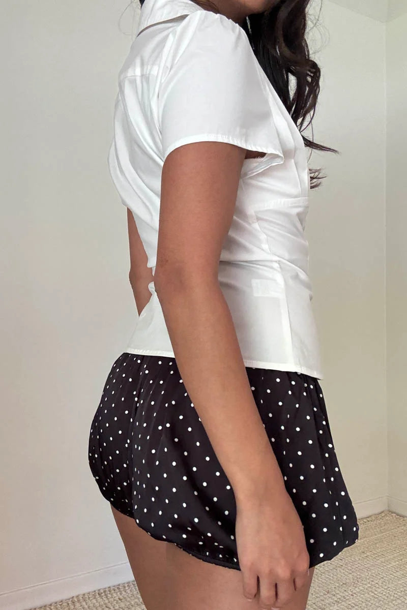 Person wearing a white shirt and black polka dot shorts against a plain background