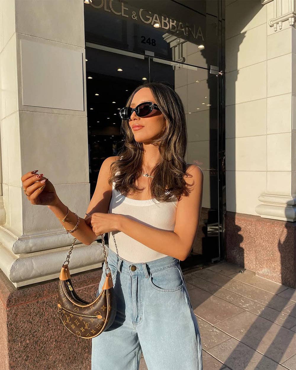 Woman in a white top and blue jeans standing in front of a Dolce & Gabbana store.