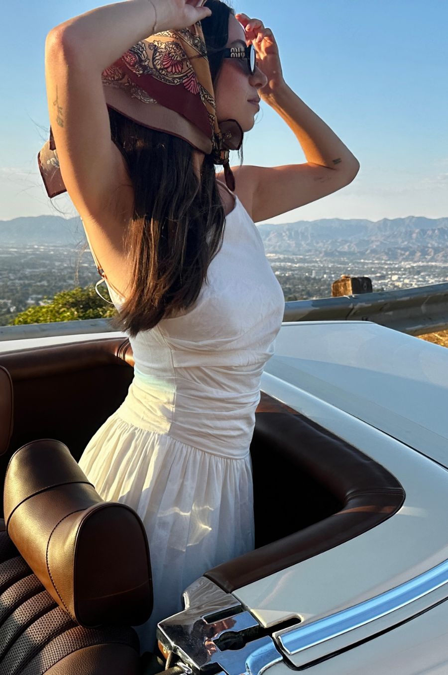 Woman in a white dress sitting in an open-top car with a scenic background