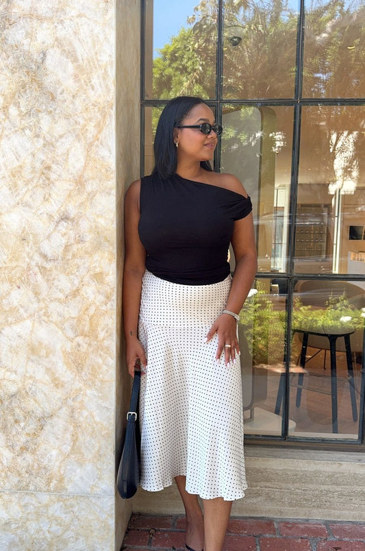 Woman in black top and white skirt standing against a textured wall with glass doors.